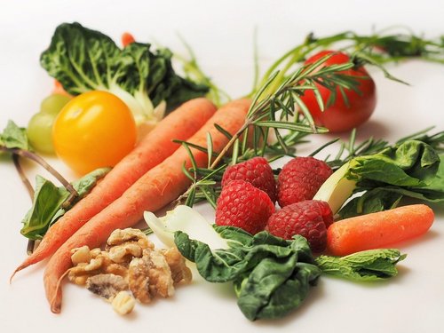 Verschiede Gemüse- und Obstsorten wie Möhren, Salat und Himbeeren liegen auf einem Tisch. 
