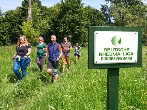 Gruppe von Menschen beim Nordic Walken, im Vordergrund Schild vom Deutschen Rheumaliga Bundesverband