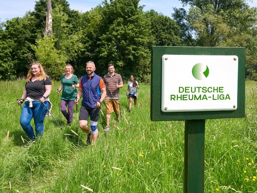 Gruppe von Menschen beim Nordic Walken, im Vordergrund Schild mit der Aufschrift "Deutsche Rheumaliga Bundesverband"