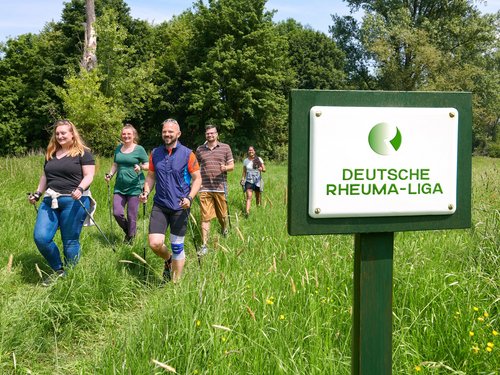 Gruppe von Menschen beim Nordic Walken, im Vordergrund Schild mit der Aufschrift "Deutsche Rheumaliga Bundesverband"